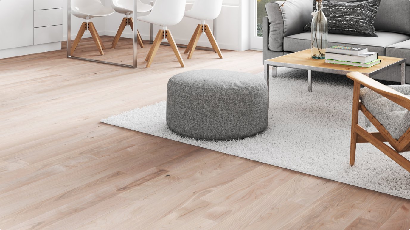Modern living room featuring the trade-pro-hero light wood flooring, a round gray pouf placed on a white rug, and a wooden coffee table situated next to a gray sofa. The dining area with white chairs is visible in the background.