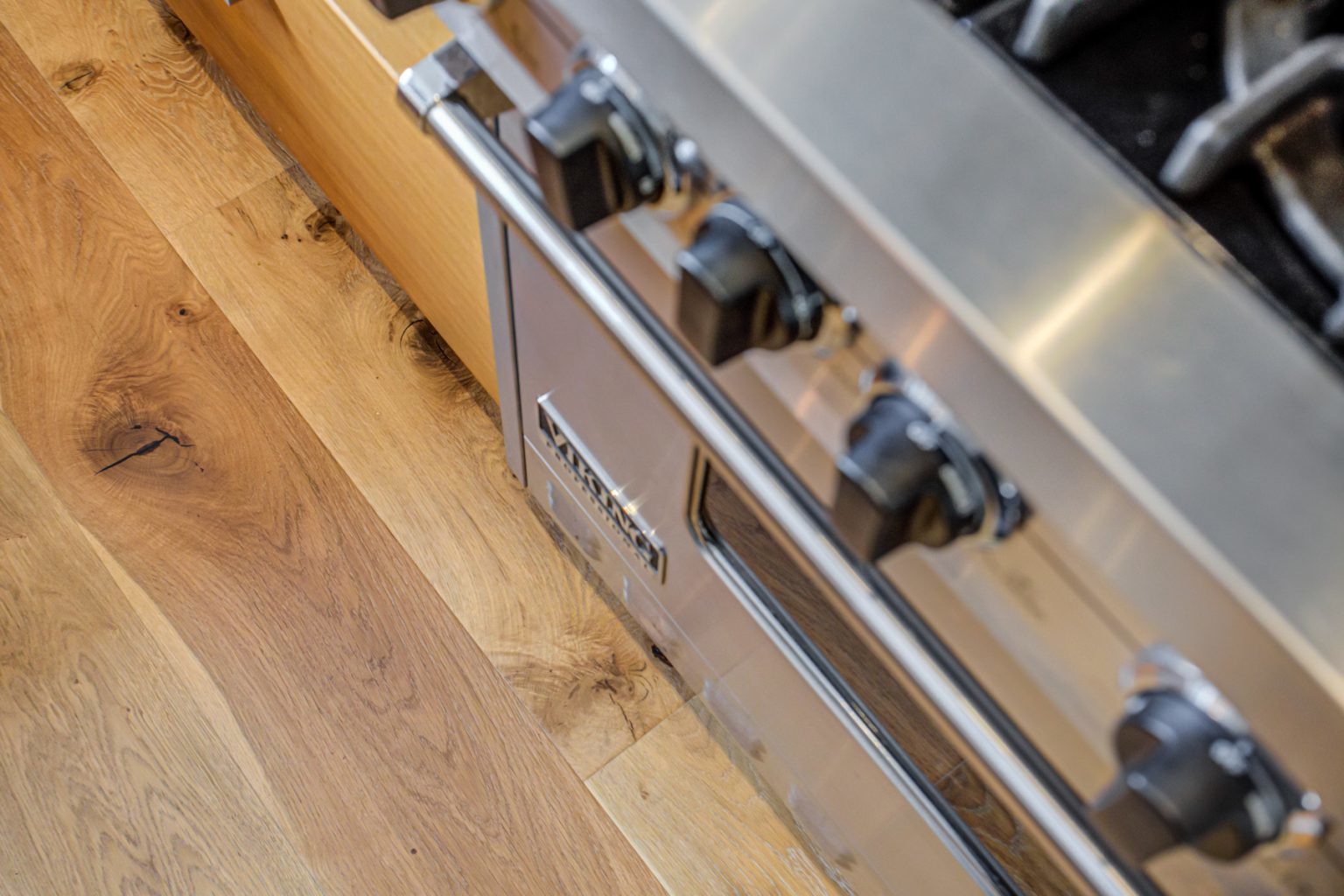 Close-up of an artists retreat1 stainless steel oven with black control knobs, adjacent to a hardwood floor.