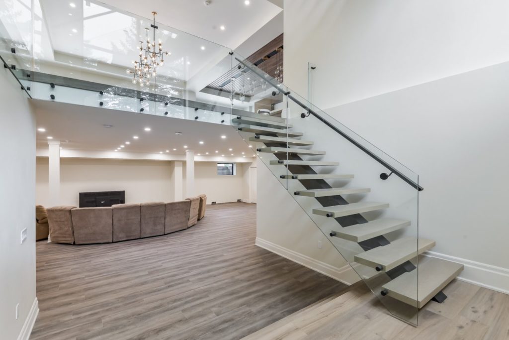 A front foyer opens into the grand room of a home. A glass staircase is off to the right, a family room is in the middle. The floor displays Fuzion's Classical Elegance Hardwood collection.