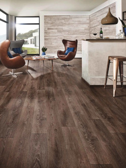 A modern living room featuring Laminate-m wooden flooring, two brown chairs, a coffee table, a bar with stools, and large windows offering a scenic view.