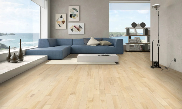 A modern living room with a Natural-Maple-m floor, blue sectional sofa, and minimalist decor. Large windows offer a view of the ocean and the sky.